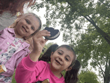 two little girls are holding up a cookie in a park