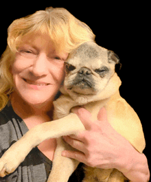 a woman holds a pug dog in her arms