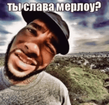 a man with a beard wearing a hat is smiling in front of a landscape with the caption " ты слава мерлоу "