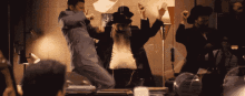 a group of people are dancing in a room and one of them is wearing a black hat