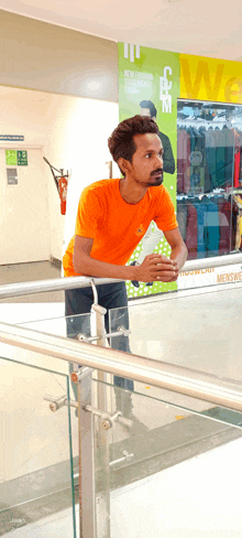 a man in an orange shirt leans on a railing in front of a sign that says menswear