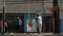 a man is swinging a bat in front of a chain link fence and a sign that says ' a ' on it