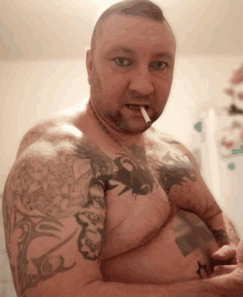 a shirtless man with tattoos on his arm and chest is smoking a cigarette