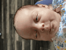 a baby wearing a floral blanket looks down at the camera