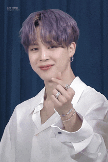 a man with purple hair is wearing a white shirt and a ring on his finger