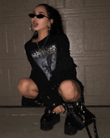 a woman wearing sunglasses and a shirt that says ' apocalypse ' on it is squatting down