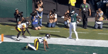 a football player in a green jersey is running with the ball while a player in a yellow jersey is kneeling on the field .