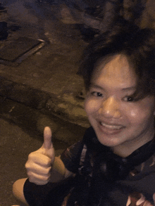 a young man giving a thumbs up while sitting on the ground