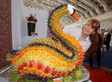 a woman is standing next to a swan made out of fruit