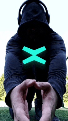 a man wearing headphones and a black hoodie has a blue x on his shirt