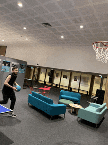 a man is playing ping pong in a living room with a basketball hoop in the background