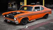 an orange muscle car is parked on the side of the road in front of a building .