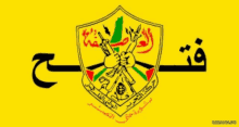 a yellow shield with arabic writing on it and a hand holding a gun