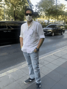 a man wearing sunglasses and a mask stands on a sidewalk in front of a miracle mall