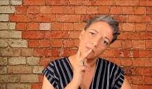 a woman in a black and white striped shirt is thinking in front of a red brick wall