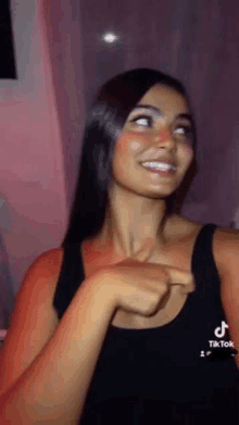 a woman in a black tank top is smiling and pointing at herself .