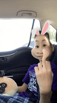 a boy wearing bunny ears is sitting in a car and giving the middle finger