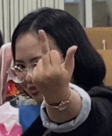 a woman wearing glasses is giving the middle finger while sitting at a table .