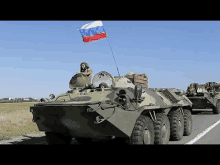 a soldier is sitting in the cockpit of a military vehicle with a russian flag flying from the top .