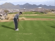 a man is swinging a golf club at a golf ball on a golf course with mountains in the background .