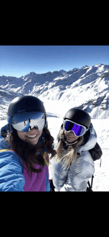 two women wearing helmets and goggles pose for a picture in the snow