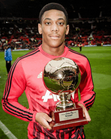 a man in a red adidas jersey holds a trophy on a soccer field