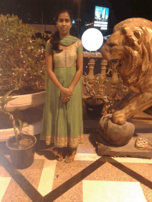 a woman in a green dress stands in front of a lion statue