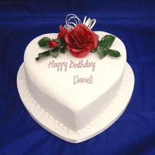 a white heart shaped birthday cake with a red rose on top