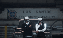 two men standing in front of a los santos sign