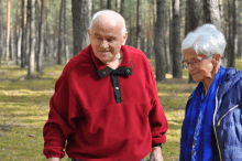 a man in a red sweater and a woman in a blue jacket are walking through a forest