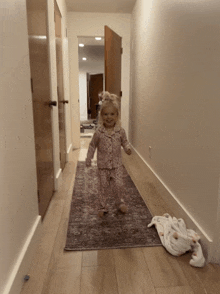 a little girl walking down a hallway with a blanket on the floor