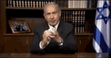 a man in a suit is sitting at a desk in front of a flag with a star of david on it