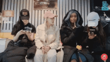 a group of women sitting next to each other looking at their cell phones with a vlive logo in the corner