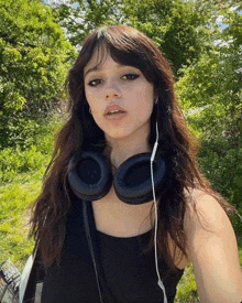 a woman wearing headphones and a black tank top is standing in a field