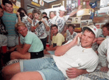 a man laying on a bed talking on a cell phone in front of a crowd of people