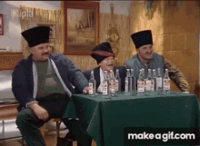 three men are sitting at a table with bottles of alcohol on it and a make a gif.com button