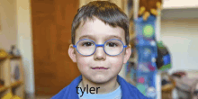 a young boy wearing blue glasses has the name tyler written on his shirt