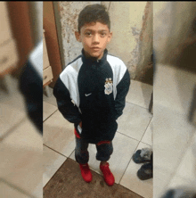 a young boy wearing a nike jacket stands in a hallway