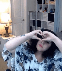 a woman in a floral shirt is making a heart shape with her hands .