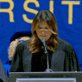 a woman in a graduation cap and gown is speaking into a microphone in front of a sign that says university