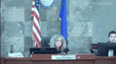 a woman is sitting in front of a computer in a courtroom with an american flag in the background .