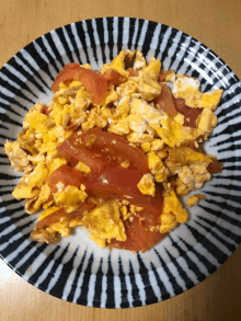 a black and white plate with scrambled eggs and tomatoes on a table