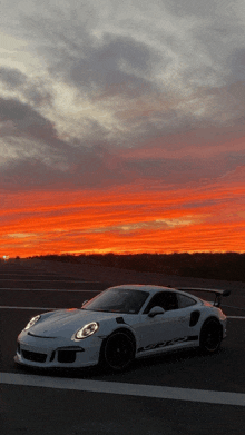 a white sports car is parked on the side of the road at sunset