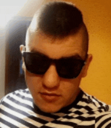 a young man wearing a striped shirt and sunglasses is taking a selfie .