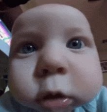 a baby with blue eyes is making a funny face with his tongue sticking out .