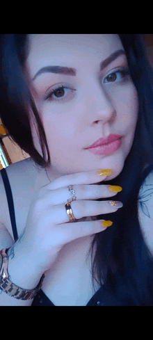 a woman with long black hair and yellow nails is taking a selfie .