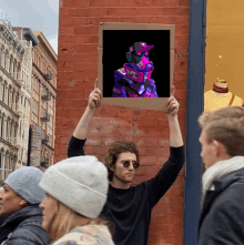 a man holds up a cardboard sign with a picture of a man in a hat and headphones on it