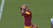 a football player wearing a maroon jersey and a yellow helmet holds his head