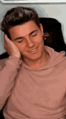 a young man wearing a pink hoodie is smiling and covering his ears with his hand