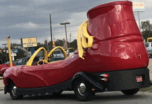 a red car that looks like a shoe is parked in front of an exxon sign